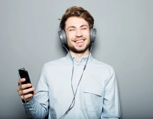 Joven usando auriculares y sosteniendo el teléfono móvil — Foto de Stock