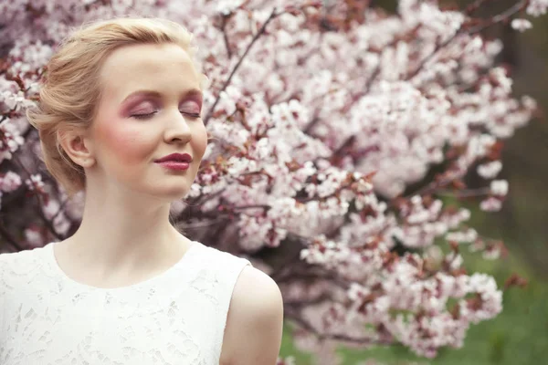 Retrato de uma bela jovem loira em um fundo de flores de cereja rosa na primavera — Fotografia de Stock