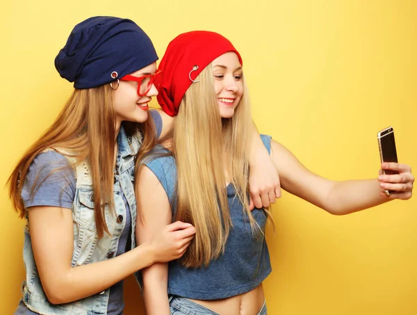 Duas jovens hipster meninas amigos tomando selfie sobre fundo amarelo — Fotografia de Stock