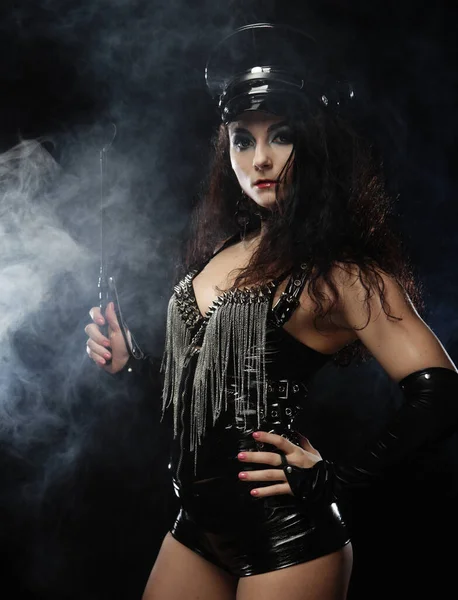 Сексуальна брюнетка жінка-коханка тримає батіг, понад темний задній план з димом — стокове фото