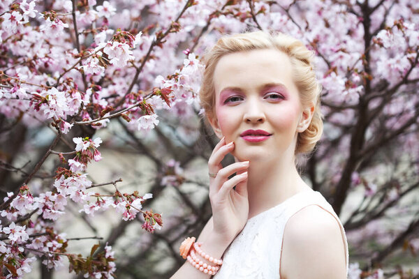 Portrait of a beautiful young blond woman on a background of pink cherry blossoms in spring