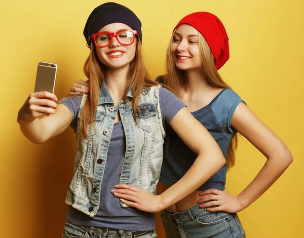 Zwei junge Hipster-Freundinnen machen Selfie vor gelbem Hintergrund — Stockfoto