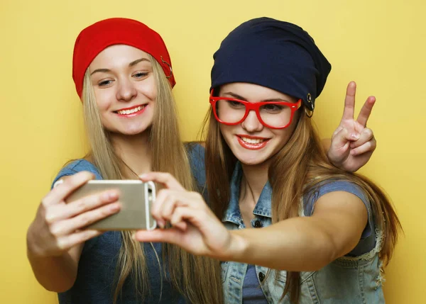 Zwei junge Hipster-Freundinnen machen Selfie vor gelbem Hintergrund — Stockfoto