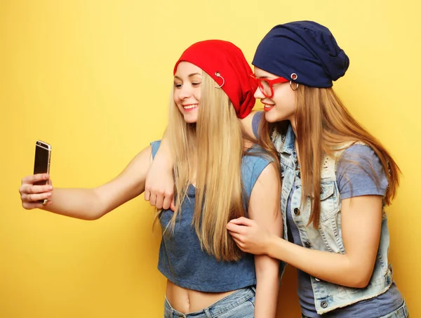 Due giovani ragazze hipster amici prendendo selfie su sfondo giallo — Foto Stock