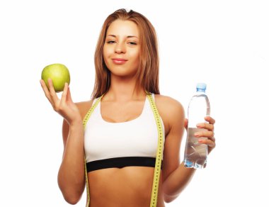 Spor yapan genç bir kadın, beyaz arka planda soyutlanmış elma ve suyla giyiniyor.