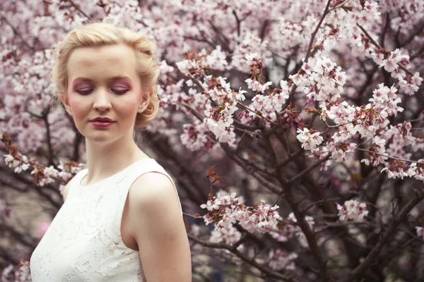 Mladá blondýna žena na pozadí růžové třešňové květy na jaře — Stock fotografie