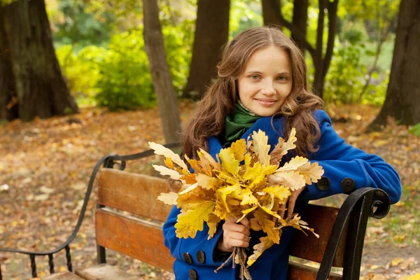 Vrouw met herfstbladeren zittend op bank — Stockfoto