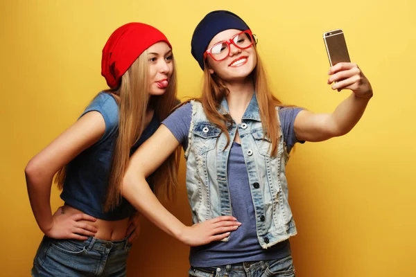 Dwa młody hipster dziewczyny przyjaciele biorąc selfie na żółtym tle — Zdjęcie stockowe