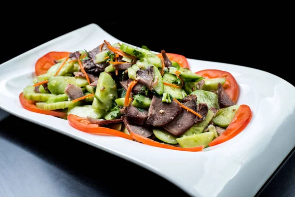 Chinese cuisine, boiled beef with cucumber and tomato in white plate on black background