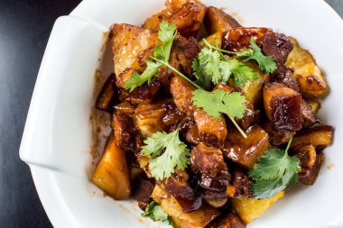 Siyah arka plan üzerine beyaz plaka tatlı soslu genç patates ile Çin sığır eti güveç