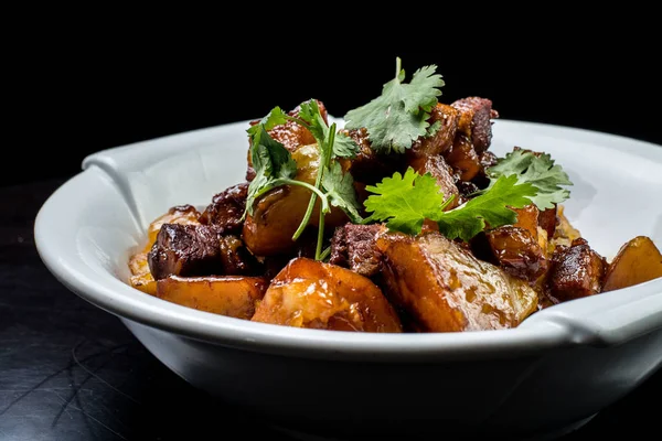 Siyah arka plan üzerine beyaz plaka tatlı soslu genç patates ile Çin sığır eti güveç