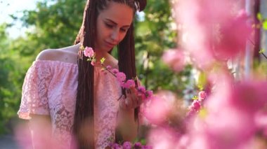 Genç casual giyinen kız bardaklarda sakura çiçekler ve gülümseyerek kameraya kokuyor. Bahar kavramı yüzüne odaklan. Ağır çekim.