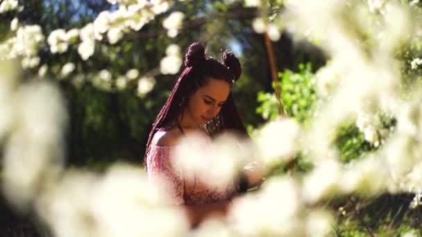 Jong casual gekleed meisje in glazen ruikt sakura bloemen en glimlacht in de camera. Focus op gezicht voorjaar concept. Slow motion. — Stockvideo
