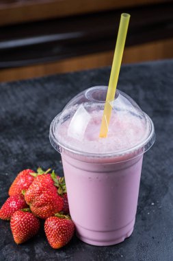 Çilekli süt karanlık bir arka plan üzerinde saman ile götürmek için