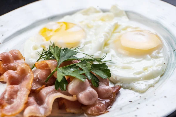 Scrambled eggs and bacon in a white plate on a dark background close-up. Omelet