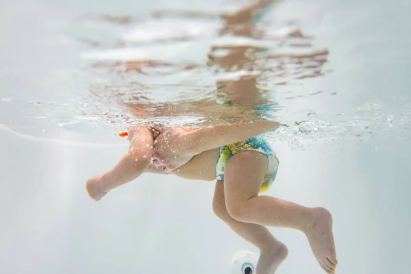 Ein kleines Kind schwimmt unter Wasser. Das Baby ist mit Tauchen beschäftigt. — Stockfoto