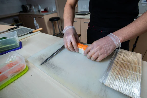 Kook handen maken Japanse sushi roll. Japanse chef-kok aan het werk bereidt heerlijke sushi roll met paling en avocado. Eetlust Japans voedsel. — Stockfoto