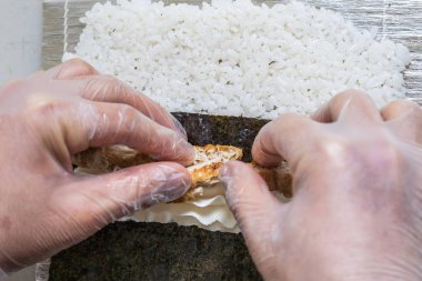 Japon suşisi yapan el yapımı bir aşçı. Japon şef işteki lezzetli suşi rulosunu yılan balığı ve avokado ile hazırlıyor. Japon yemekleri iştah açıcı..