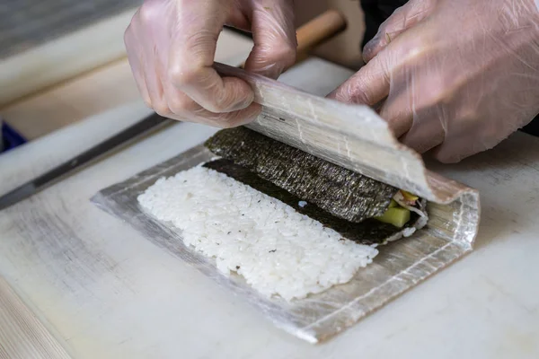 Руки печуть, готуючи японці суші. Японський шеф-кухар на роботі готує смачний суші-рол з вугром і авокадо. Вид на японці.. — стокове фото