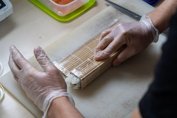 Kook handen maken Japanse sushi roll. Japanse chef-kok aan het werk bereidt heerlijke sushi roll met paling en avocado. Eetlust Japans voedsel. — Stockfoto