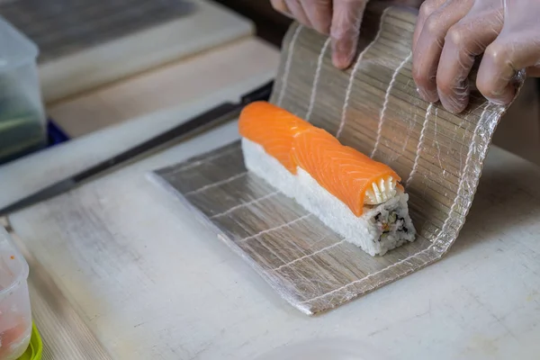 Cocinar las manos haciendo rollo de sushi japonés. Chef japonés en el trabajo preparando delicioso rollo de sushi con anguila y aguacate. Apetitivo comida japonesa. — Foto de Stock