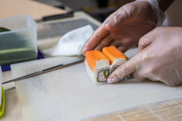 Cook hands making japanese sushi roll. Japanese chef at work preparing delicious sushi roll with eel and avocado. Appetizing japanese food.