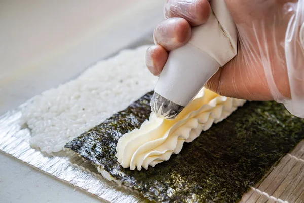 Cook hands making japanese sushi roll. Japanese chef at work preparing delicious sushi roll with eel and avocado. Appetizing japanese food. — Stock Photo, Image