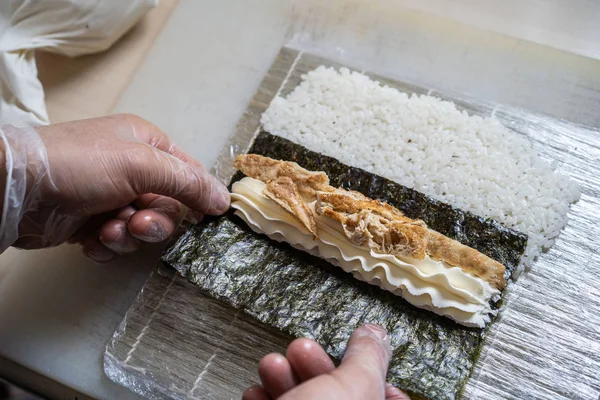 Cook hands making japanese sushi roll. Japanese chef at work preparing delicious sushi roll with eel and avocado. Appetizing japanese food. — Stock Photo, Image