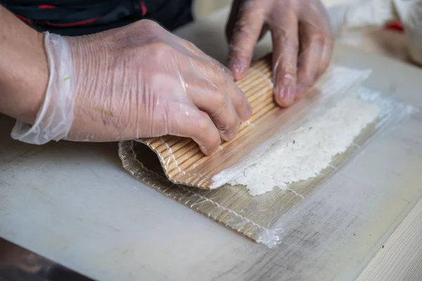 Cook hands making japanese sushi roll. Japanese chef at work preparing delicious sushi roll with eel and avocado. Appetizing japanese food. — Stock Photo, Image