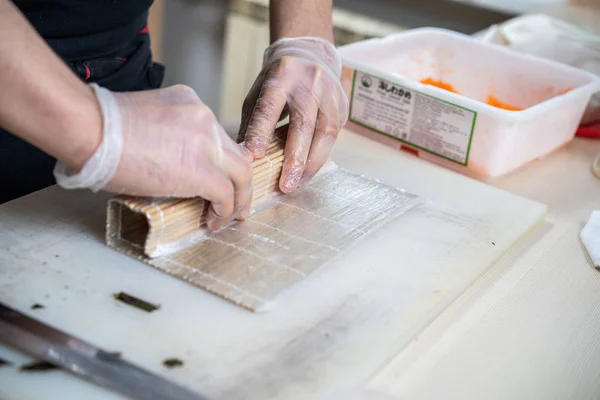 Cozinhe as mãos fazendo rolo de sushi japonês. chef japonês no trabalho preparando delicioso rolo de sushi com enguia e abacate. Comida japonesa apetitosa. — Fotografia de Stock