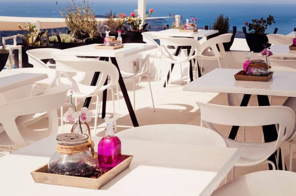Greece, Santorini. Restaurant with served table in seafront of Aegean sea on Santorini Cyclades island with breathtaking, amazing and unbelievable view on the water and embankment of Oia Ia village. - Image