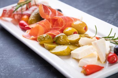 Salatalık turşusu ve pişirilmiş et silindirleriyle servis edilen zeytinler.