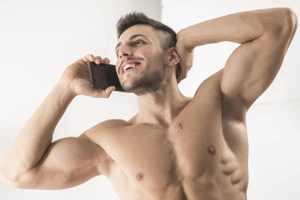 ポーズ ハンサムな上半身裸の若い運動男性と白い背景の上の Holdiong 携帯電話 — ストック写真