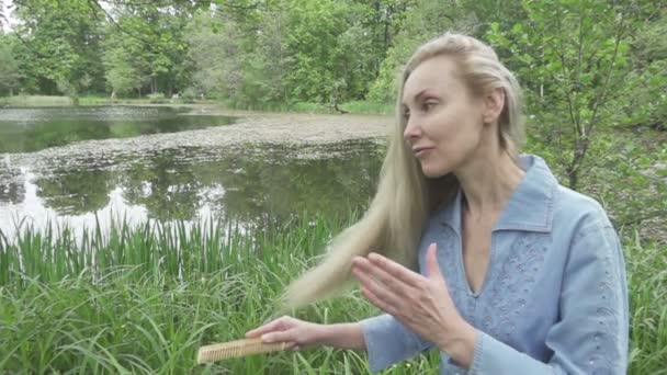 A fiatal nő combs egy hosszú tisztességes haj-haj, a háttérben a tó. Lassú mozgás — Stock videók
