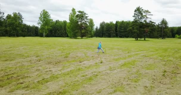 Вид з дрона на жінку в блакитній куртці і джинсах, що йдуть на полях з скошеною травою — стокове відео
