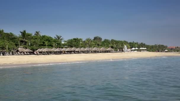 Onde del mare caldo scorrono sulla spiaggia sabbiosa del resort tropicale con ombrelloni e chaise longue — Video Stock