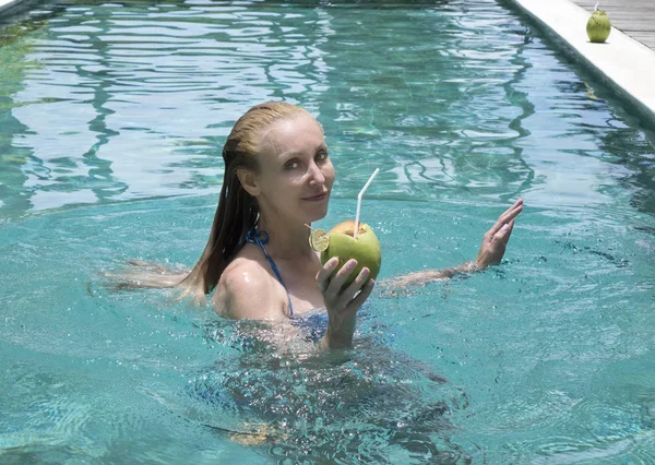 这位年轻貌美的女士 留着一头长发 穿着泳衣 在游泳池里喝着椰子鸡尾酒 — 图库照片