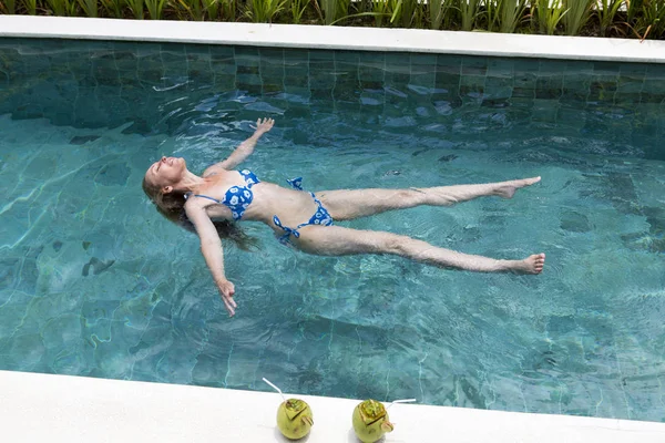 这个快乐而纤细的女人躺在游泳池的水面上休息 — 图库照片