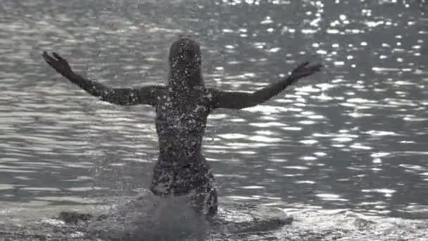 La silueta de la joven esbelta mujer feliz que se para en el mar y salpica las manos de agua.cámara lenta — Vídeos de Stock