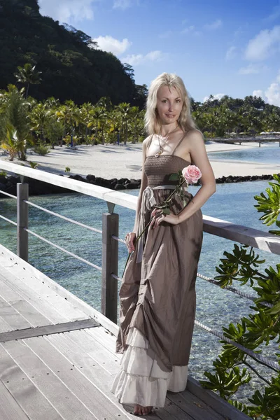 The young beautiful woman with a rose on a wooden path at the sea, tropics