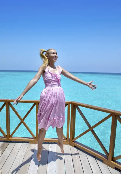年轻美丽的女孩跳在粉红色的太阳裙在别墅的水下伞 马尔代夫的平台上 — 图库照片