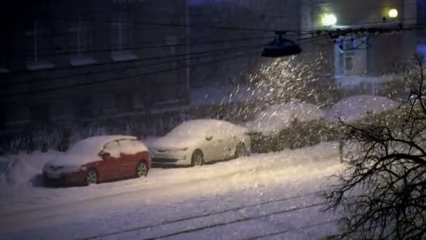 Auto innevate in città, nevicate notturne illuminate da un lampione in città — Video Stock