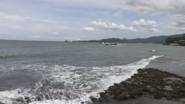 Узбережжя тропічного моря в сонячний день, Хвилі біжать на узбережжі з чорними каменями — стокове відео