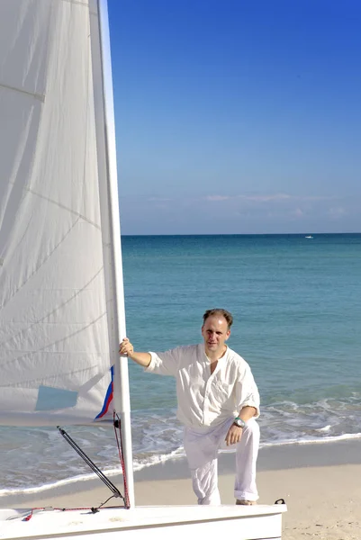 Cuba. A man on the blue sea next to a boat with a sai