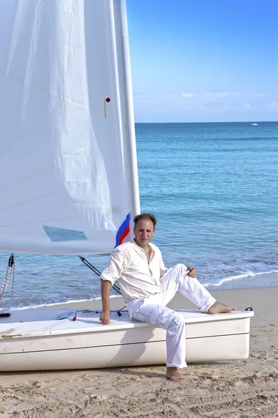 Cuba. A man on the blue sea next to a boat with a sai