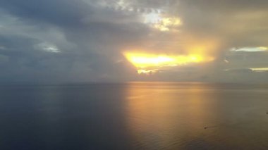 Tropik denizde gün doğumu. Drone'dan aero çekimi, palmiye ağaçlarıyla sahil, güneş bulutların arasından parlayacak, denizde balıkçı tekneleri