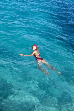 Tahiti 'de mavi denizde yüzen kırmızı mayolu genç bir kadın.