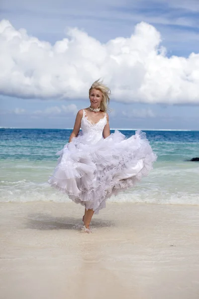 年轻的美丽的女人在一个长长的白色新娘礼服沿着蓝色海的边缘运行 — 图库照片