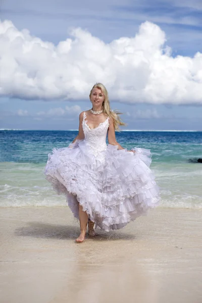 年轻的美丽的女人在一个长长的白色新娘礼服沿着蓝色海的边缘运行 — 图库照片