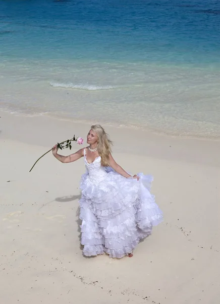 年轻的美丽的女人在一个长长的白色新娘礼服在沙滩上的蓝色Se — 图库照片